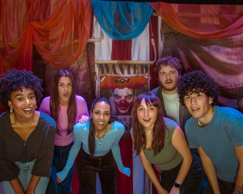 A group of friends pose in front of a "WANTED" poster. 