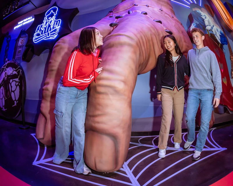 Three friends pose with the iconic Thing hand from Wednesday at Netflix House Dallas.