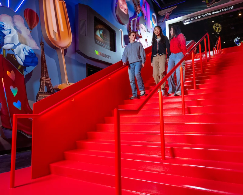 Three people walking down entrance stairs at Netflix House Dallas having fun.