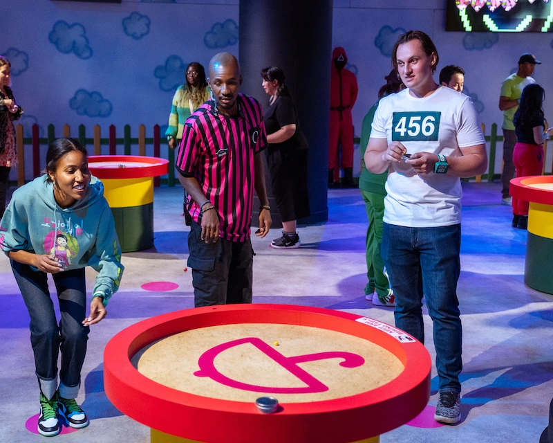 Three friends throw marbles into the hole at the interactive Squid Game experience.