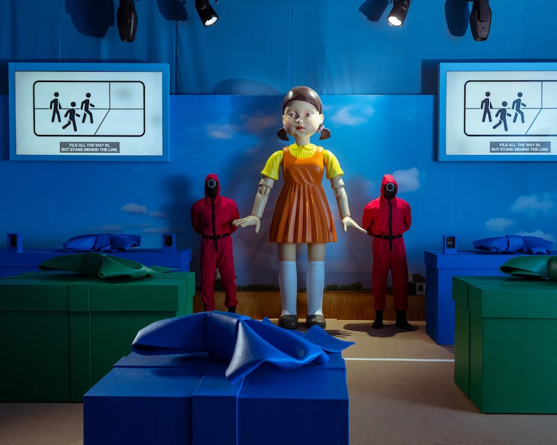 Two pink guards pose next to Young-hee in the Red Light, Green Light game of Squid Game.