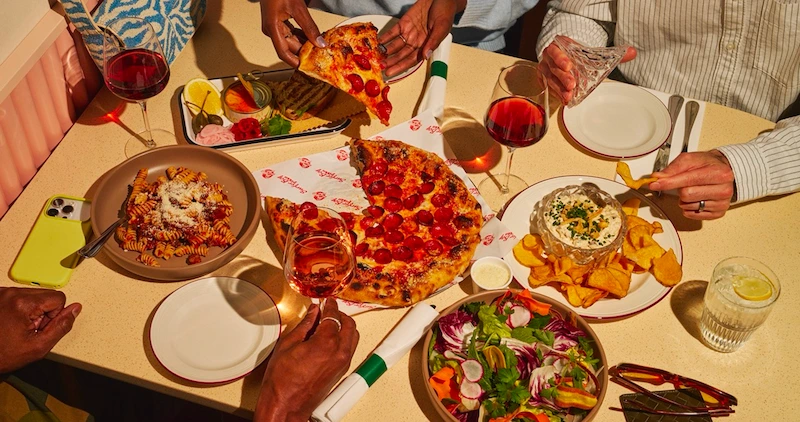 A group enjoys pizza, pasta, onion dip, salad, and wine.