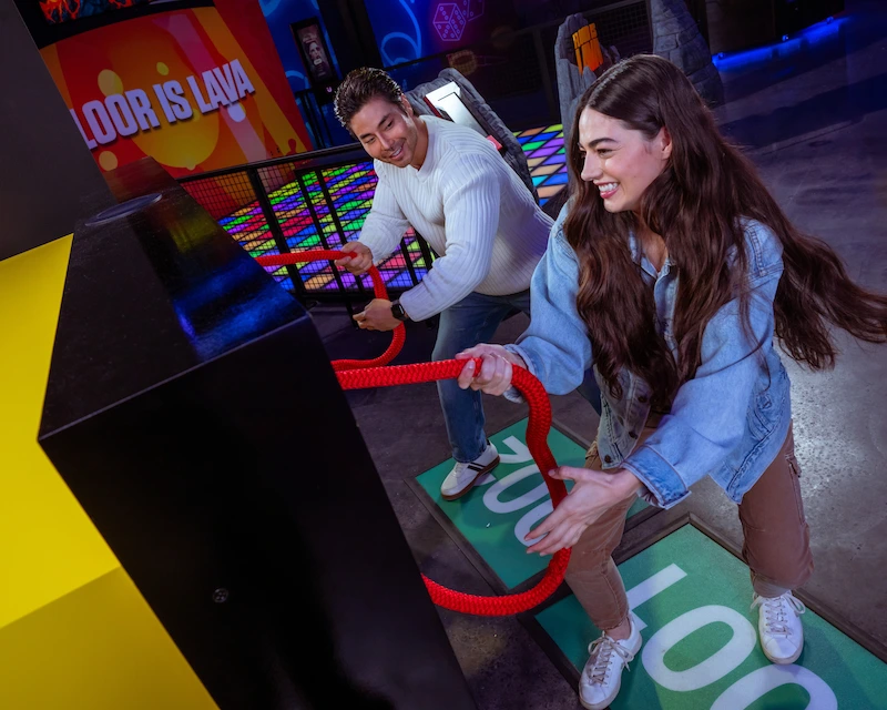 Two friends play a tug of war game at the RePLAY arcade room in Netflix House Dallas.