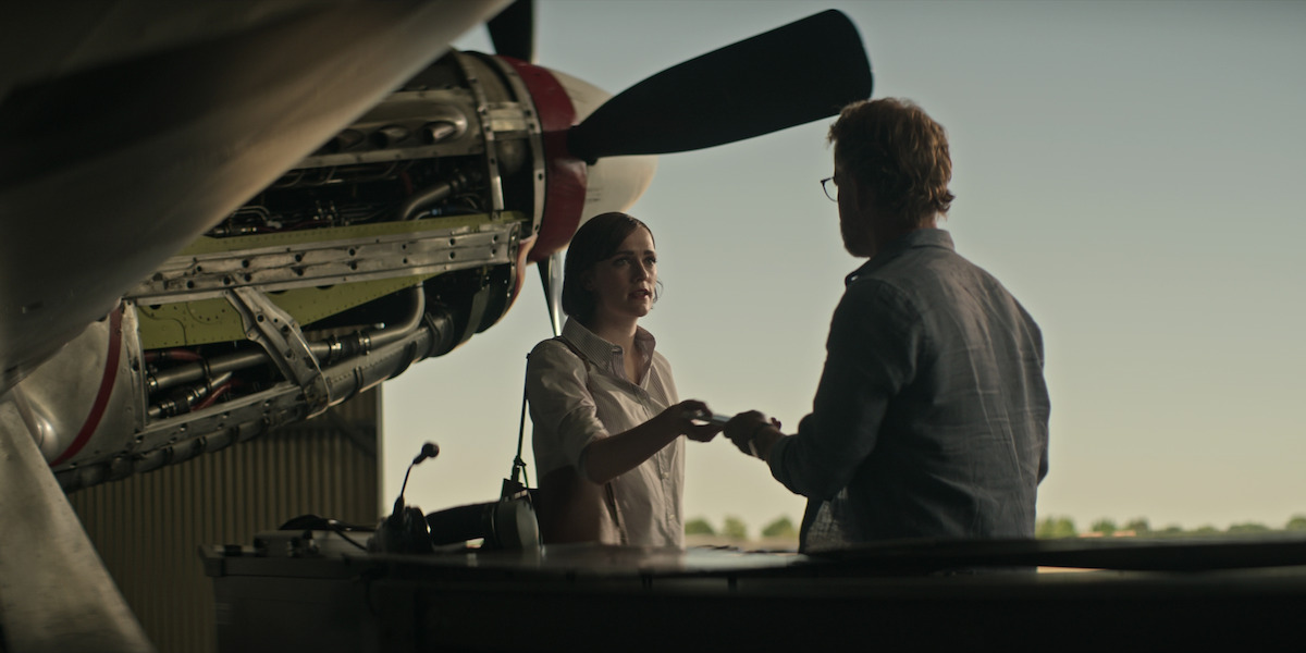 Charlotte Ritchie and Greg Kinnear speak in an airplace hangar as Kate and Tom