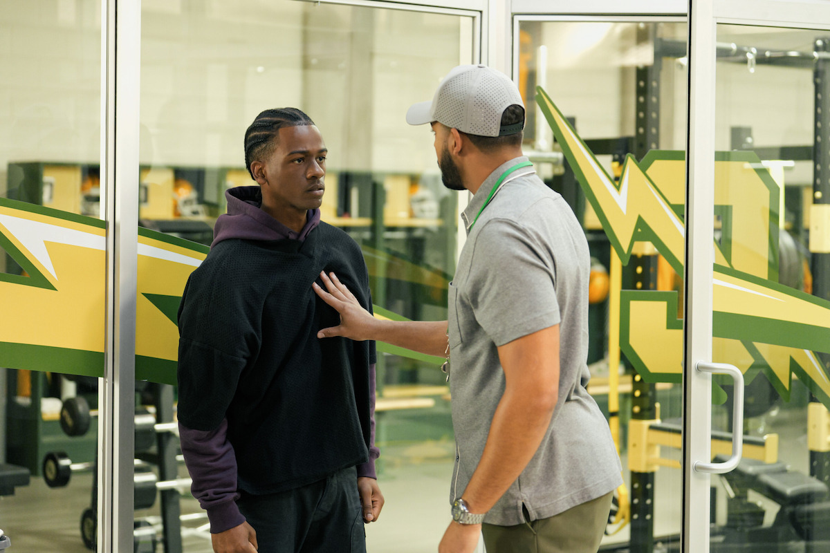 A coach admonishes a teen football player in a weight room.