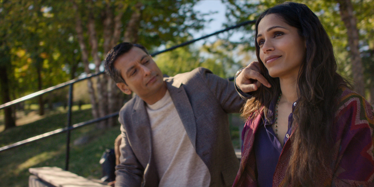 Two people sitting on outdoor steps in a park, surrounded by trees and greenery, sharing a peaceful and intimate moment together under natural daylight.