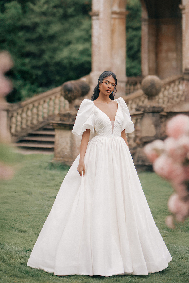 Woman in bridal dresses poses and looks off into the distance.