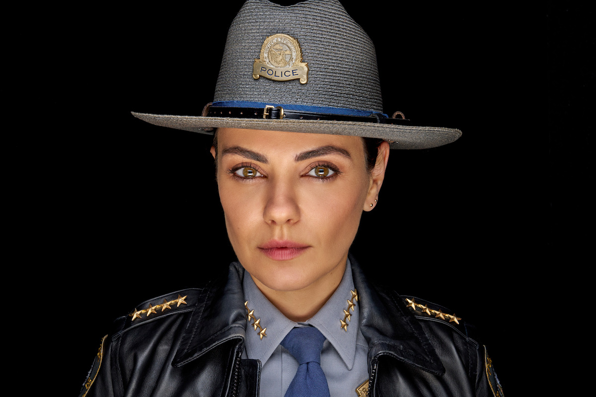 A serious female police officer in uniform and hat poses against a black background, creating a professional and authoritative mood in a studio environment.