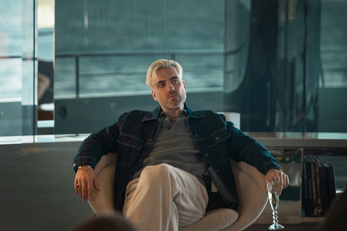 Daniel Ings sits back in a chair with a glass of champagne in one hand.