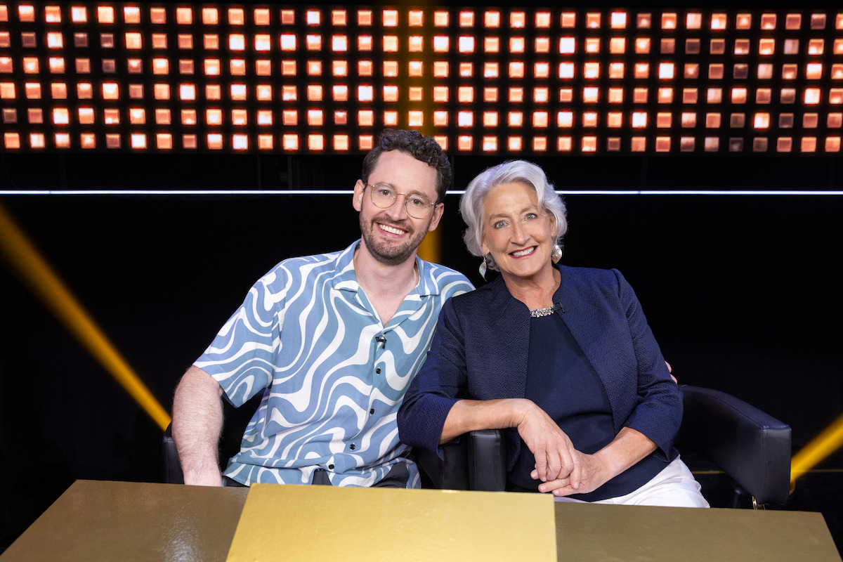 A smiling man and woman sit together at a table in a brightly lit studio with a glowing backdrop, conveying a friendly and welcoming atmosphere.