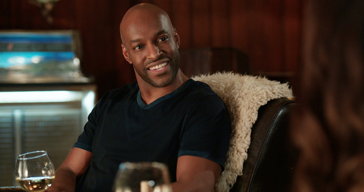 Colin Lawrence as John “Preacher” Middleton sits in a lounge chair smiling at someone.