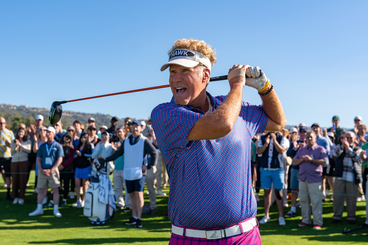 A golfer mid-swing wearing a visor, colorful shirt, and pink pants on a sunny golf course with a crowd of spectators watching in the background.