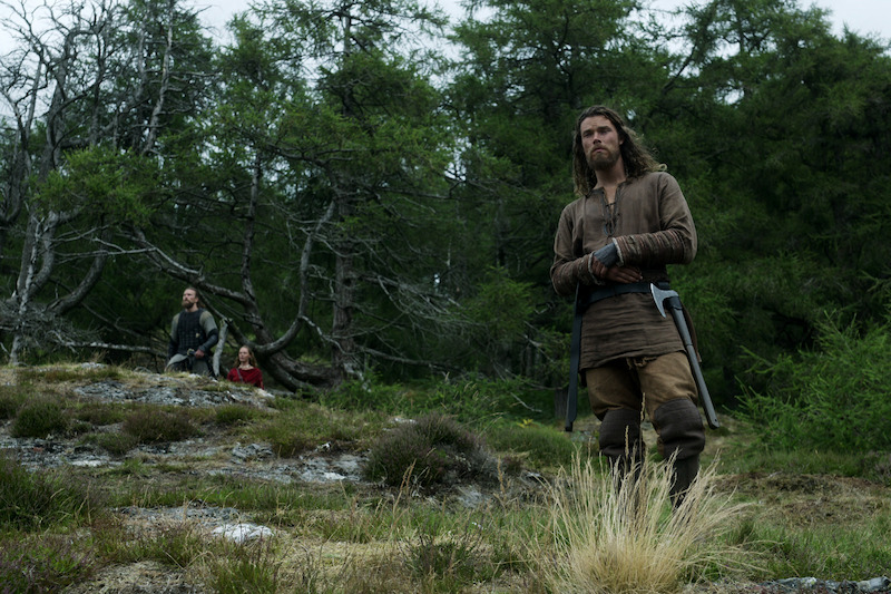 Leo Suter as Harald Sigurdsson, Frida Gustavsson as Freydis Eriksdotter, and Sam Corlett as Leif Eriksson hiking through a dense forest. 