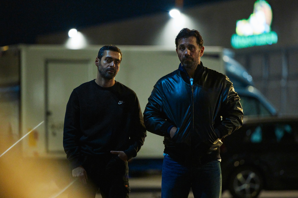 Ardalan Esmaili as Michel and Mahmut Suvakci as Rami stand together wearing black clothing in ‘The Helicopter Heist’