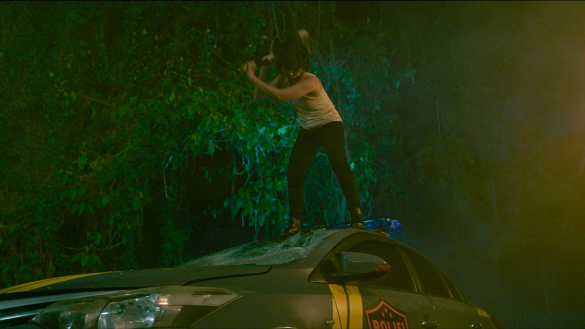 Marsha Timothy as Murni stands on top of a car and swings an axe in an image from the 2024 film ‘Monster.’