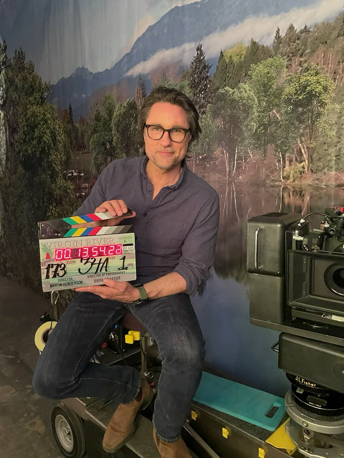 Martin Henderson behind the scenes on the Virgin River set holding a clapboard.