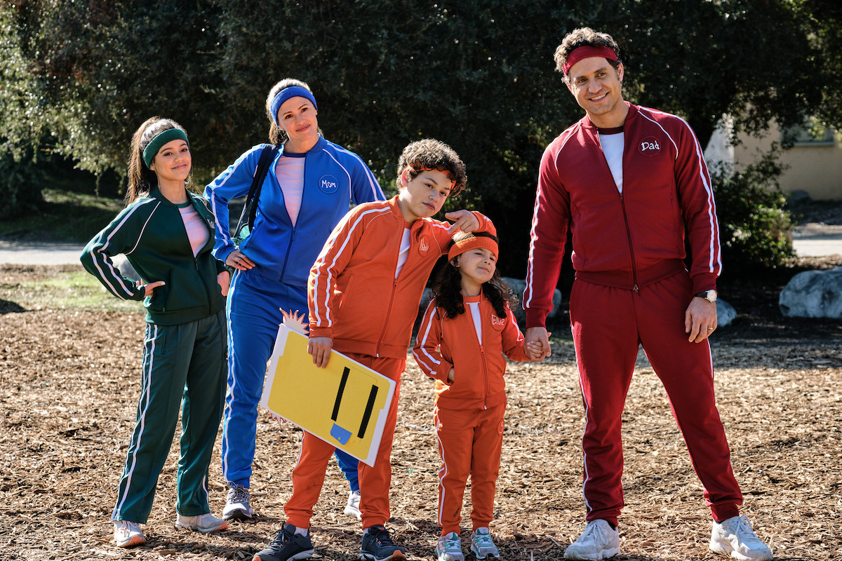 A mom, dad and three children stand in a field, all wearing tracksuits