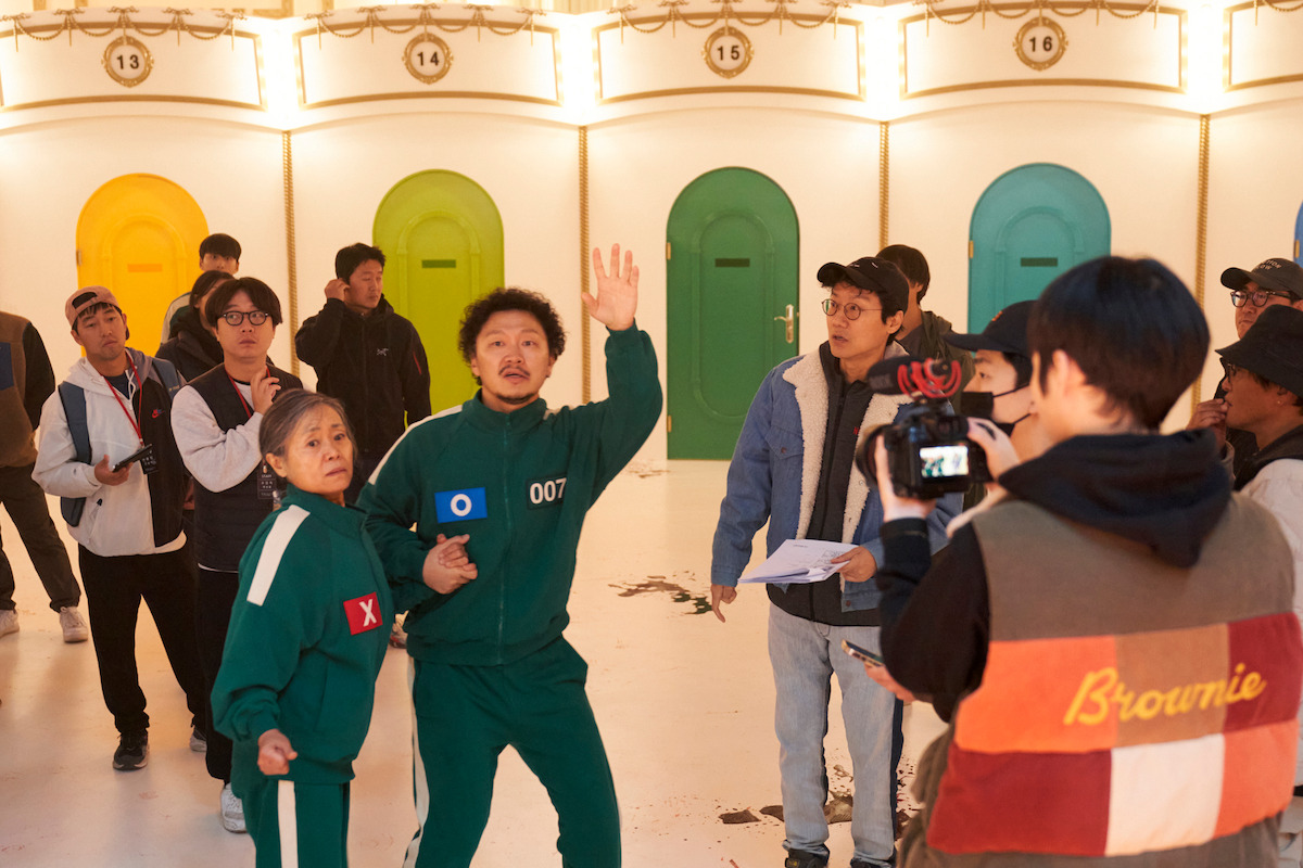 ‘Squid Game’ Season 2 set with players in green tracksuits against colorful doors.