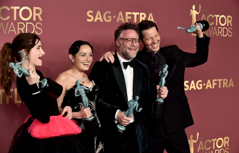 Four people dressed formally holding SAG Awards trophies and smiling on the red carpet at the SAG-AFTRA Actor Awards event, standing in front of a maroon event backdrop with gold lettering.