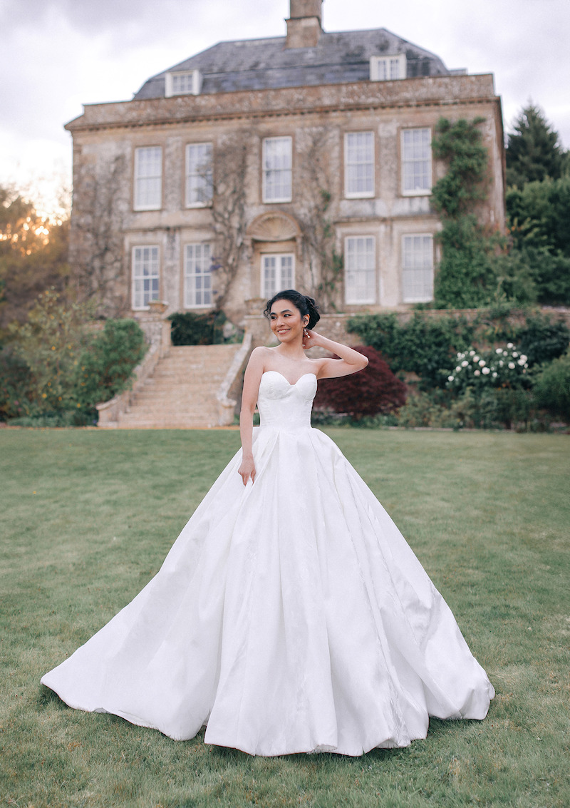 Woman in bridal dresses poses and looks off into the distance.