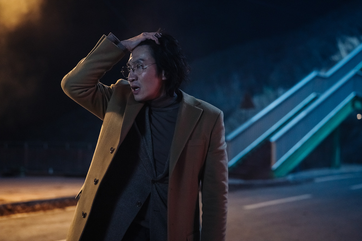 Lee Kwang-soo stands in an empty street in the dark with his hand clasping the top of his head in an image from the series ‘Karma.’