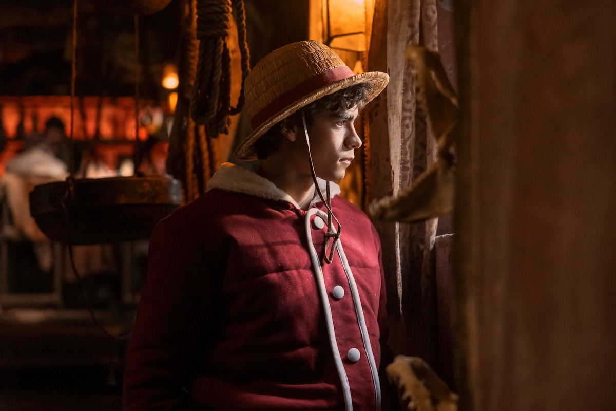 luffy-de-one-piece-live-action-olhando-pela-janela-com-chapéu-de-palha-e-casaco-vermelho-em-cena-da-série-da-netflix