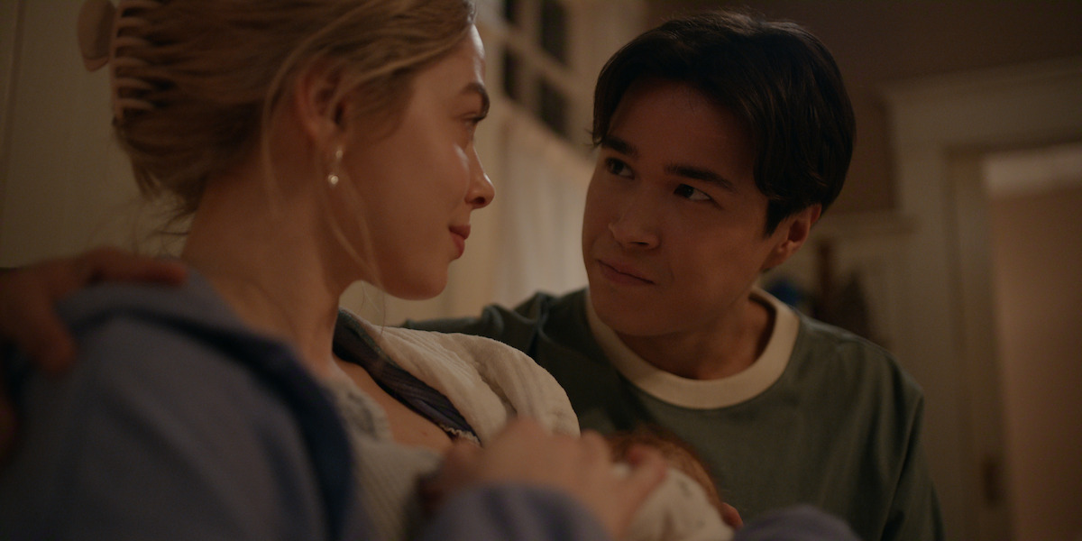 A young couple sits closely together indoors, gazing at each other lovingly in a warmly lit room, creating an intimate and tender atmosphere.