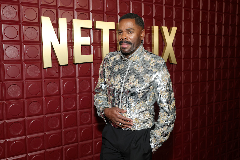 Colman Domingo stand in front of a red backdrop.