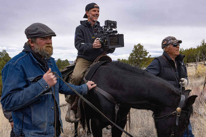 Behind the scenes photo with director holding camera on a horse.  