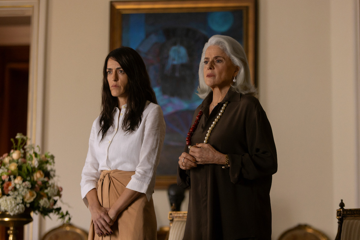Duas mulheres posam lado a lado em frente a um quadro de cor azul