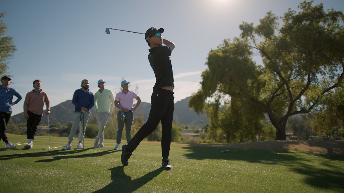 Min Woo Lee takes a swing with his golf club with onlookers behind him.