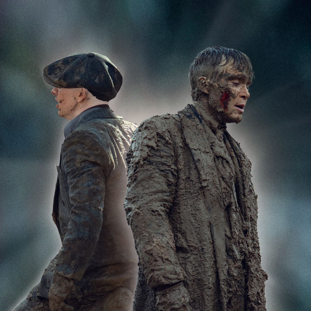 Un hombre cubierto de barro espeso se encuentra al aire libre frente a una pared de ladrillos erosionados, vestido con ropa andrajosa y embarrada. El entorno parece arenoso e industrial, lo que sugiere condiciones duras o una situación intensa.