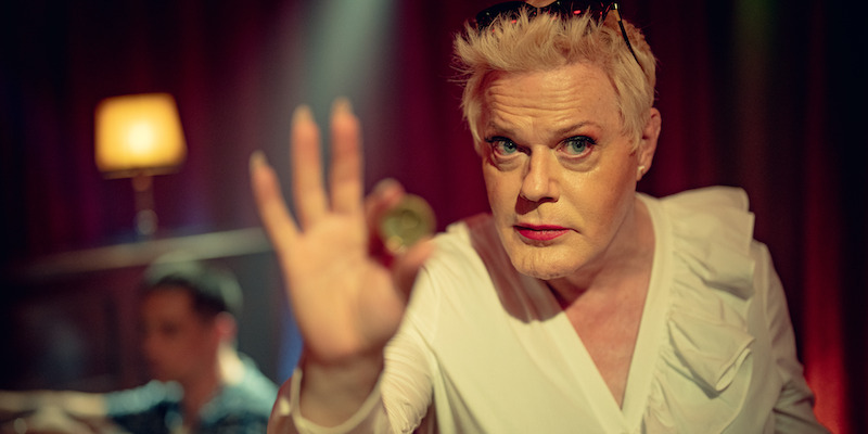 Eddie Izzard as Lachy holds up a gold coin in Season 1 of ‘Kaos’