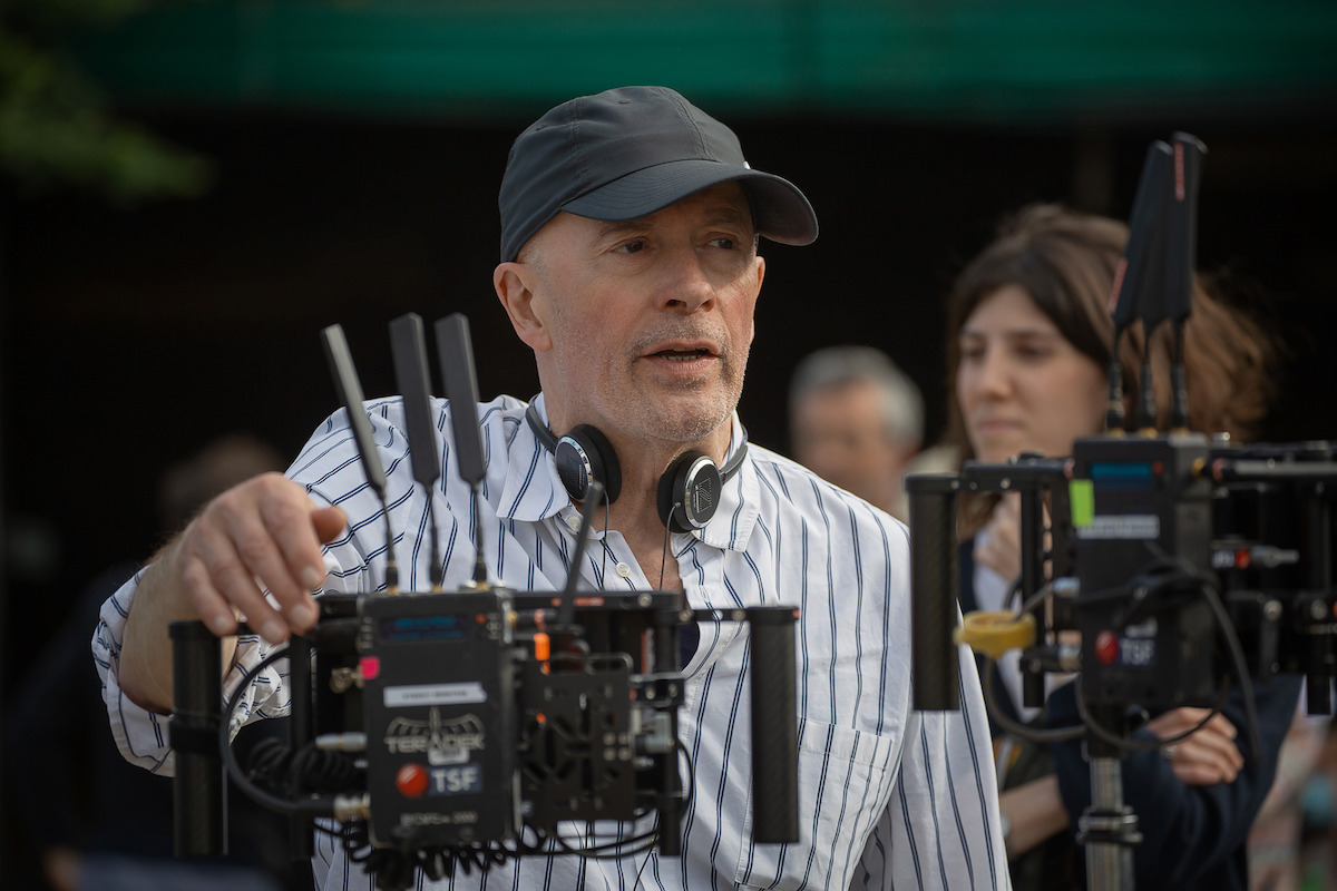 Jacques Audiard wears a striped shirt and earphones around his necklace looking like a baller on set.