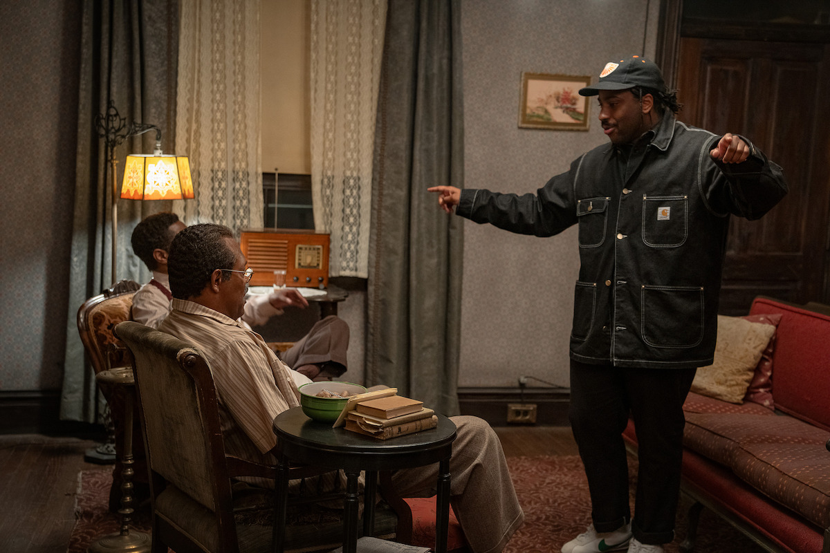 Malcolm Washington gives Corey Hawkins and Samuel L. Jackson in their living room set. Malcolm wears a trendy black chore coat.