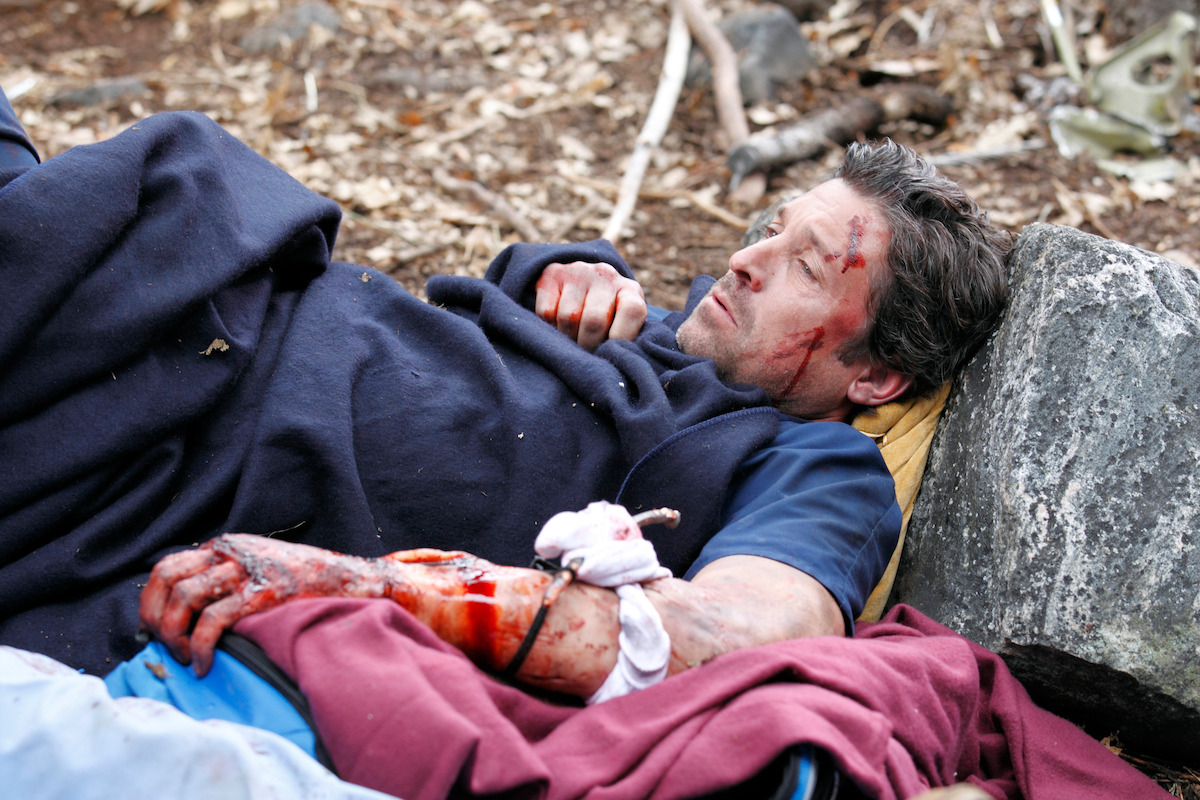 an injured man rests on the ground, while covered in a blanket. 