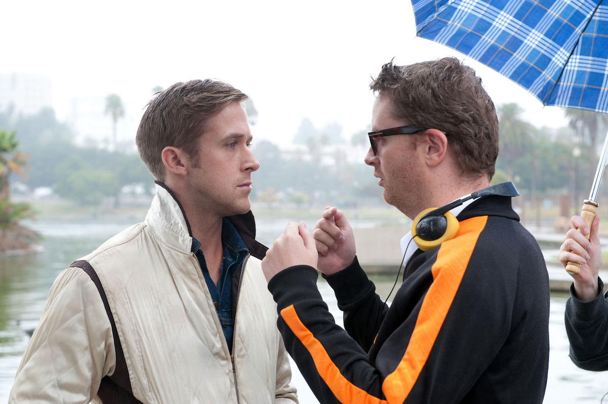 Ryan Gosling wears a white jacket and takes notes from Nicolas Winding Refn who wears a black jacket with an orange stripe.