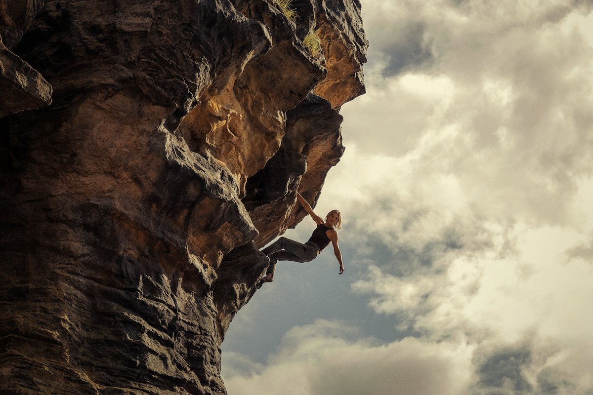 A climber hangs from a dramatic rock cliff against a partly cloudy sky, capturing a sense of adventure, challenge, and the thrill of outdoor climbing in a rugged natural environment.