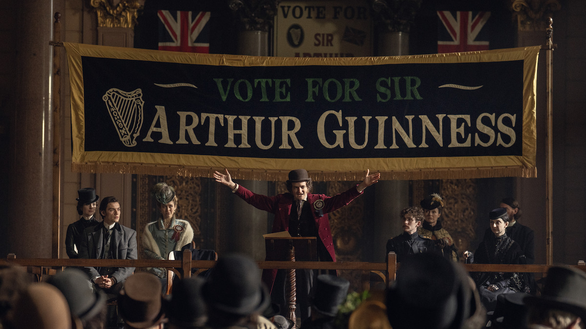 Jack Gleeson as Byron Hedges on a stage under a ‘Vote for Sir Arthur Guinness’ sign in ‘House of Guinness’ Season 1.