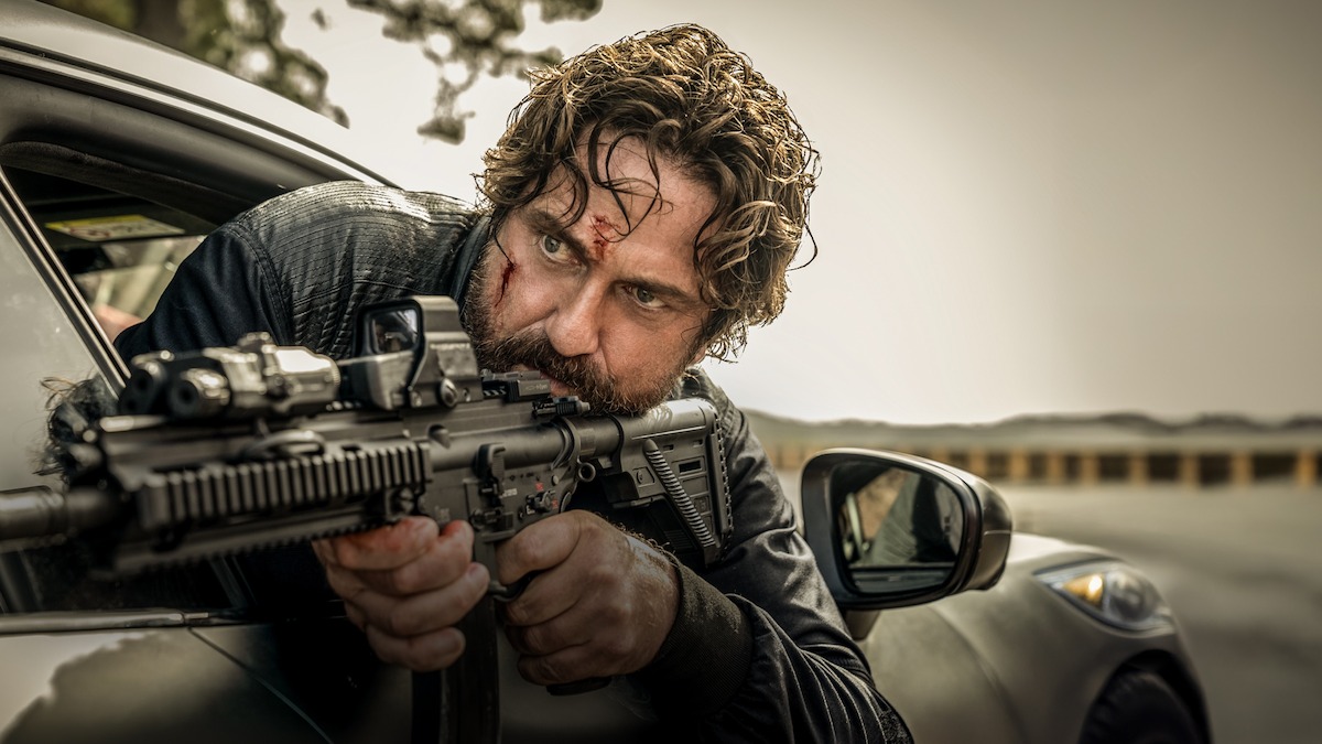 Gerard Butler wields a gun while hanging out of a car window in ‘Den of Thieves 2: Pantera.’