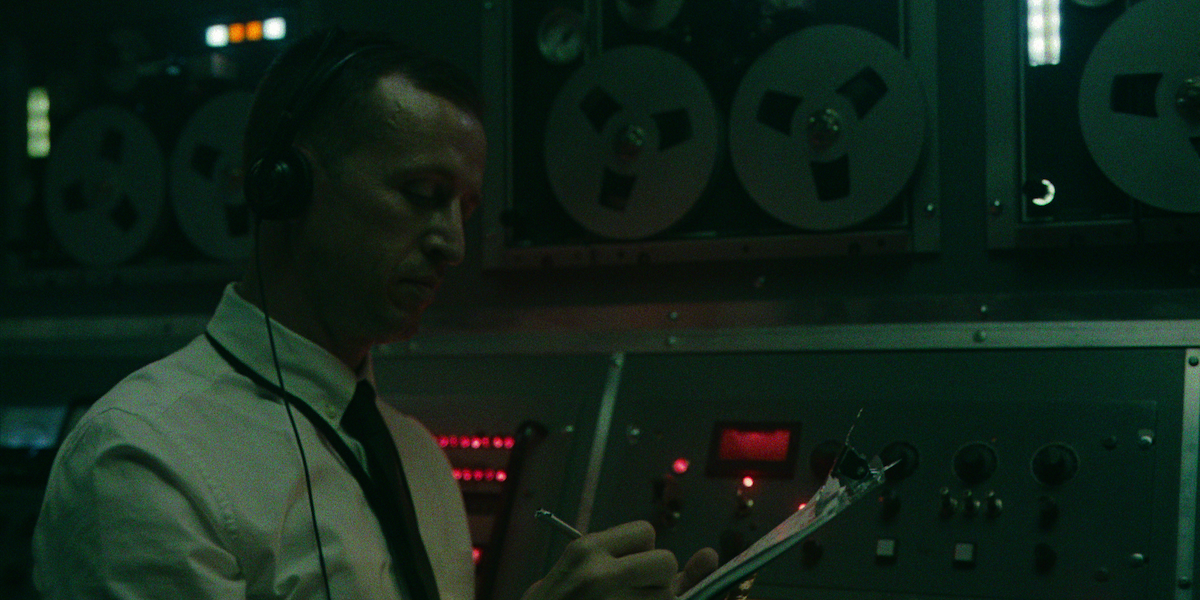 A man wearing headphones writes on his clipboard.