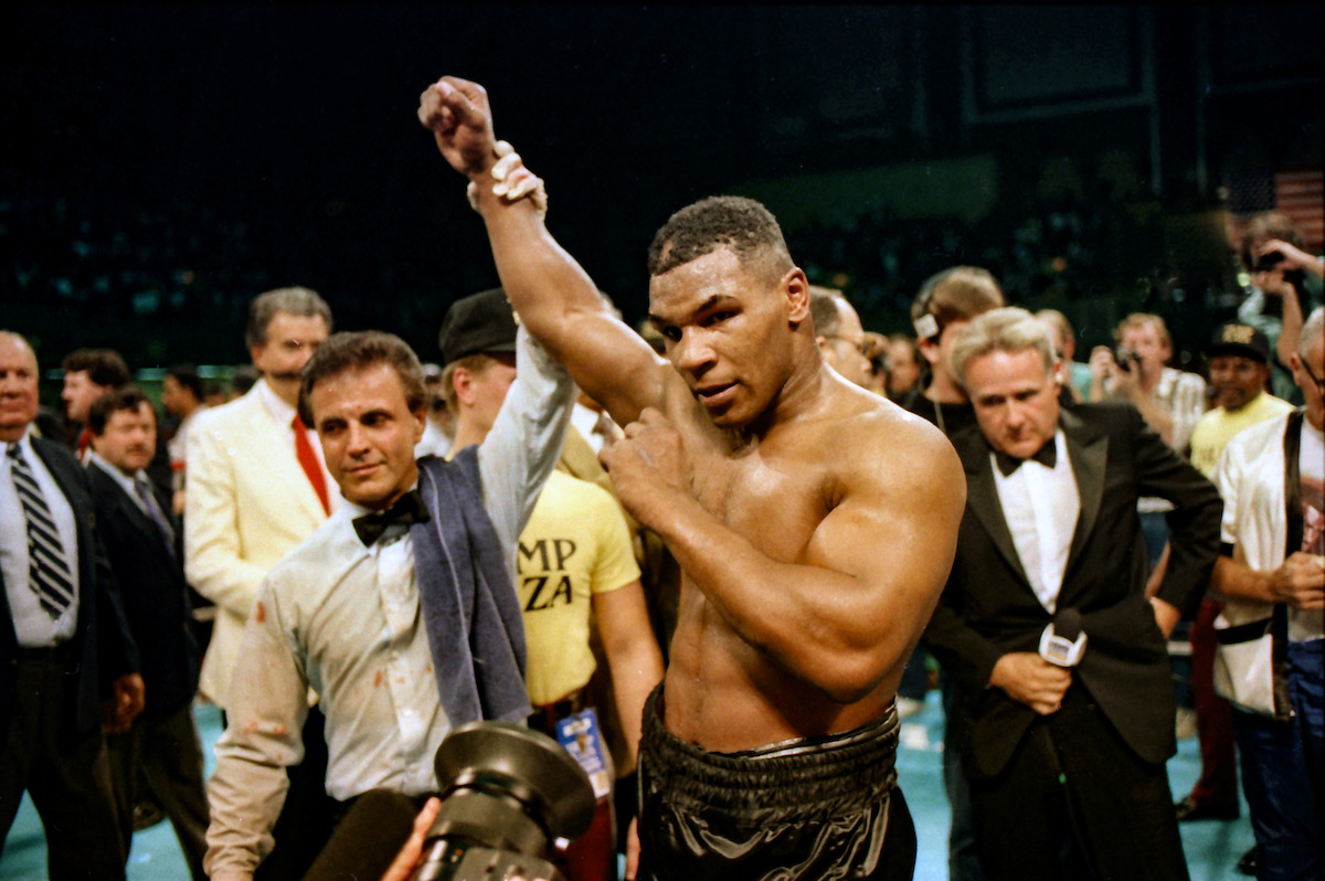 Mike Tyson with a ref raising his hand in victory in a boxing ring.