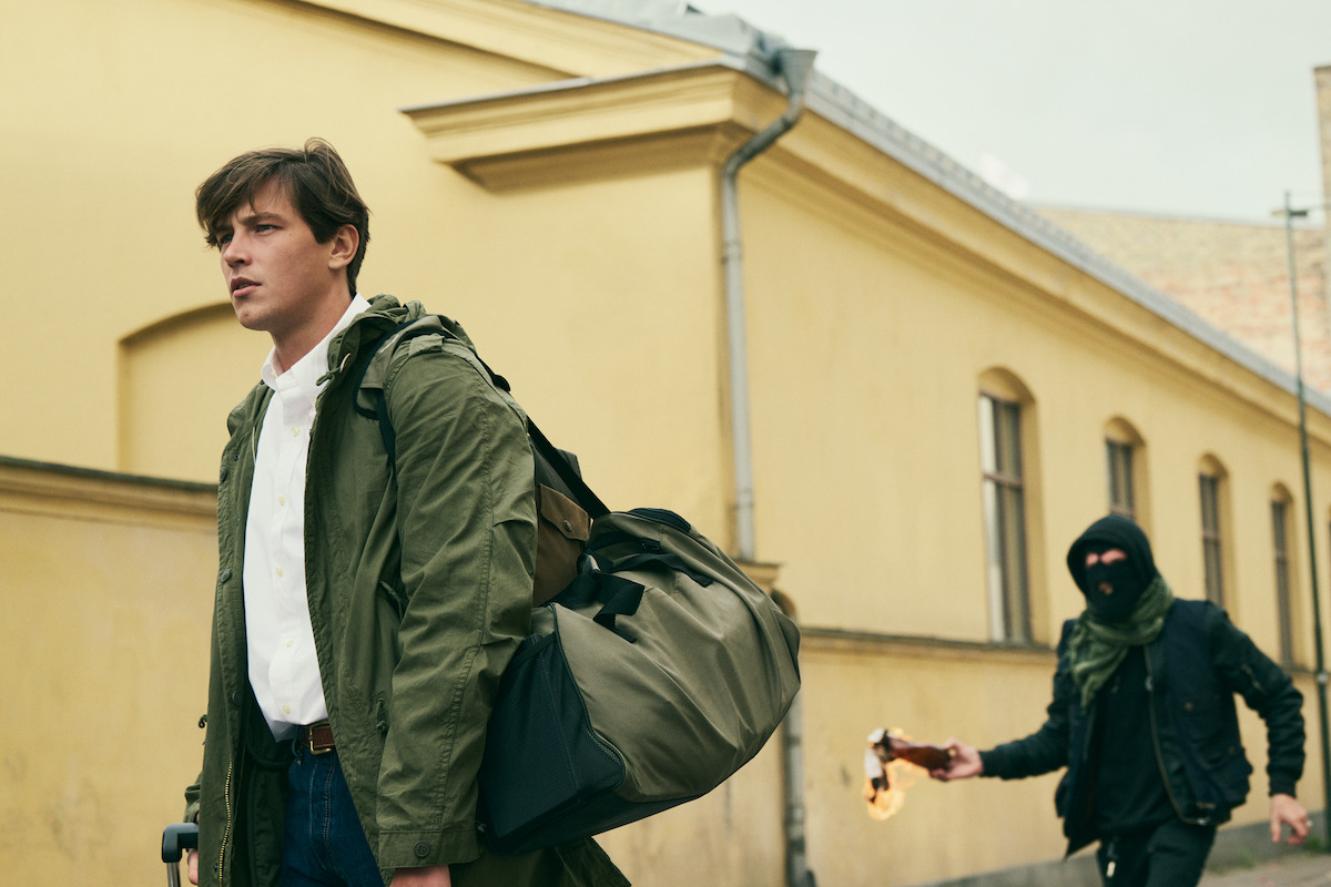 Simon Lööf as Simon walks down the street while a protest is going on behind him in a production still from An Honest Life.