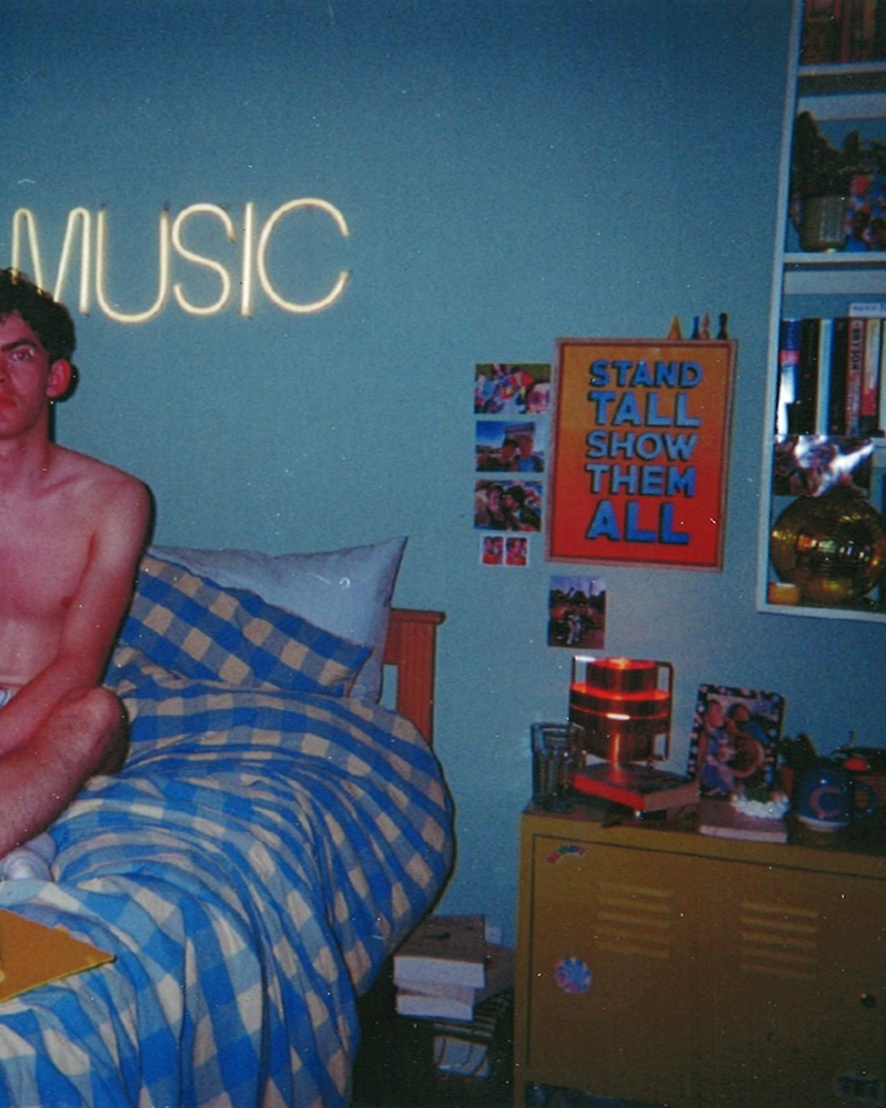 Disposable camera photo of Joe Locke as Charlie Spring sitting on a bed in a dorm room