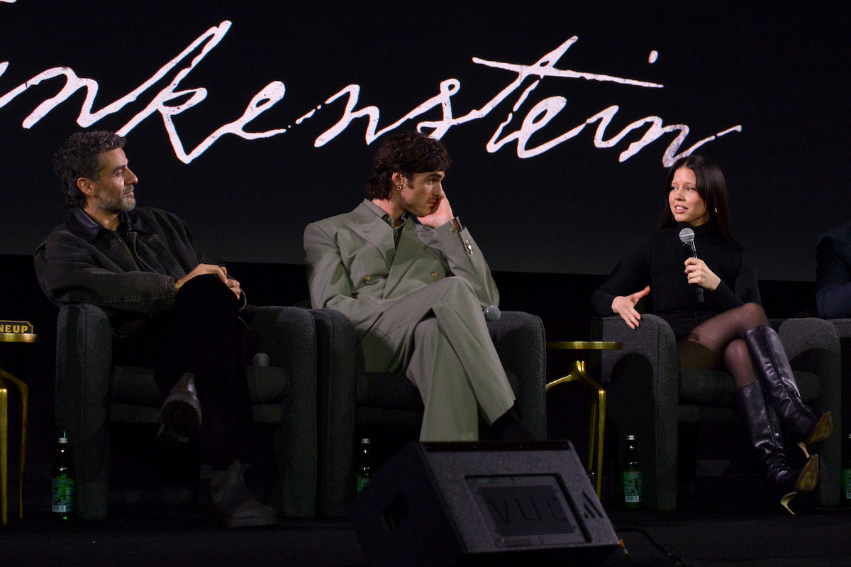 Oscar Isaac, Jacob Elordi, and Mia Goth hold mics as they speak on a panel.