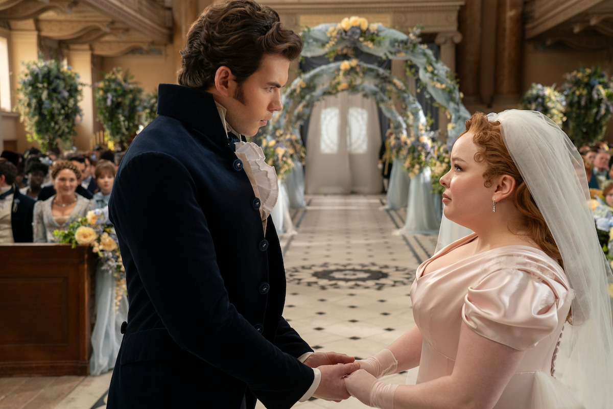 Luke Newton as Colin Bridgerton and Nicola Coughlan as Penelope Featherington stand together at their wedding in Season 3 of ‘Bridgerton’