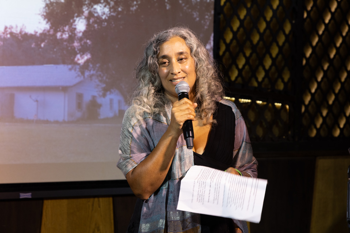 Geeta Gandbhir holds a mic while giving s speech.
