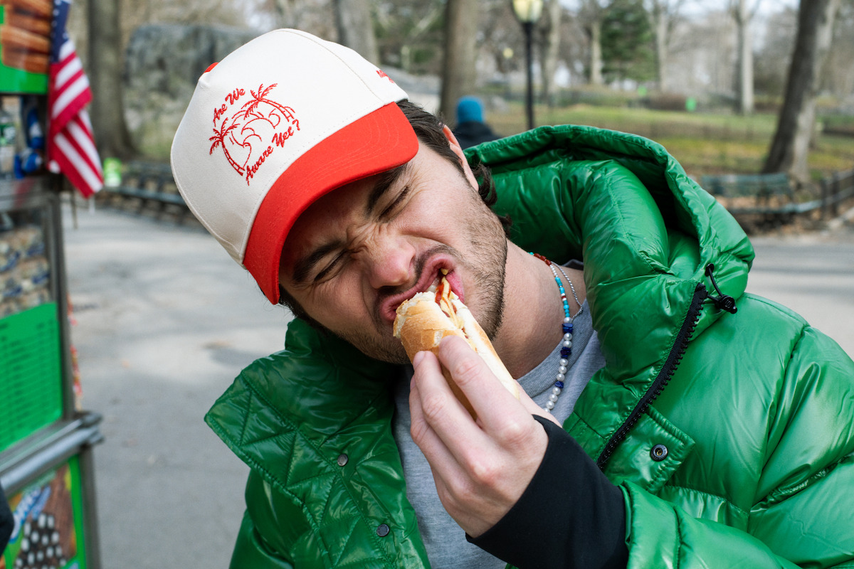 Chase Stokes in Central Park eating a hot dog.