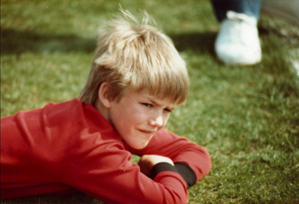 A young David Beckham lays on a football pitch.