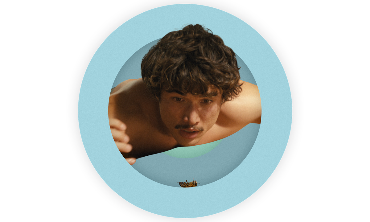 A spot photo illustration of Charles Melton as Austin as he lies on the floor shirtless and deeply concerned with the well being of a bee who has fallen to the floor in his and Ashley’s home in BEEF Season 2.